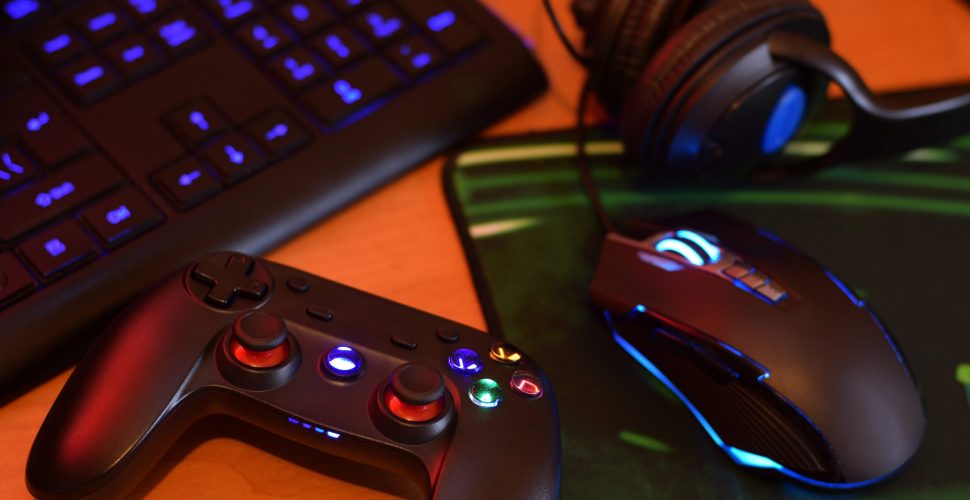 Modern gamepad and gaming mouse lies with keyboard and headphones on table in dark playroom scene close up. Lets play video games together with friends concept